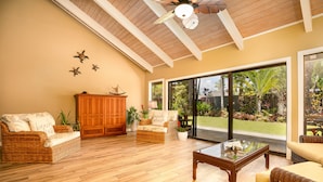 Un vaste salon doté d’un haut plafond, d’un plancher en bois, de meubles en osier et de grandes portes-fenêtres coulissantes donnant sur un jardin.