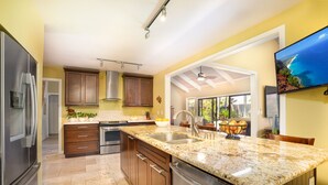 Une cuisine moderne dotée de plans de travail en granit, d’appareils électroménagers en acier inoxydable, d’armoires en bois et d’un grand îlot central avec un évier.