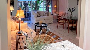 Ein Wohnzimmer mit Sofa, Couchtisch und Lampe, ein Essbereich mit Stühlen und Tisch sowie ein Blick ins Freie.