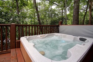A hot tub on a wooden deck surrounded by trees.
