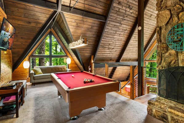 A cozy room with a pool table, a sofa, and a fireplace.