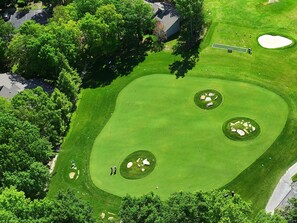Um campo de golfe com um green bem cuidado, bunkers de areia e um putting green.