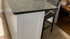 Une cuisine dotée d’un plan de travail en granit, de meubles blancs et d’un petit îlot central avec des tabourets de bar.