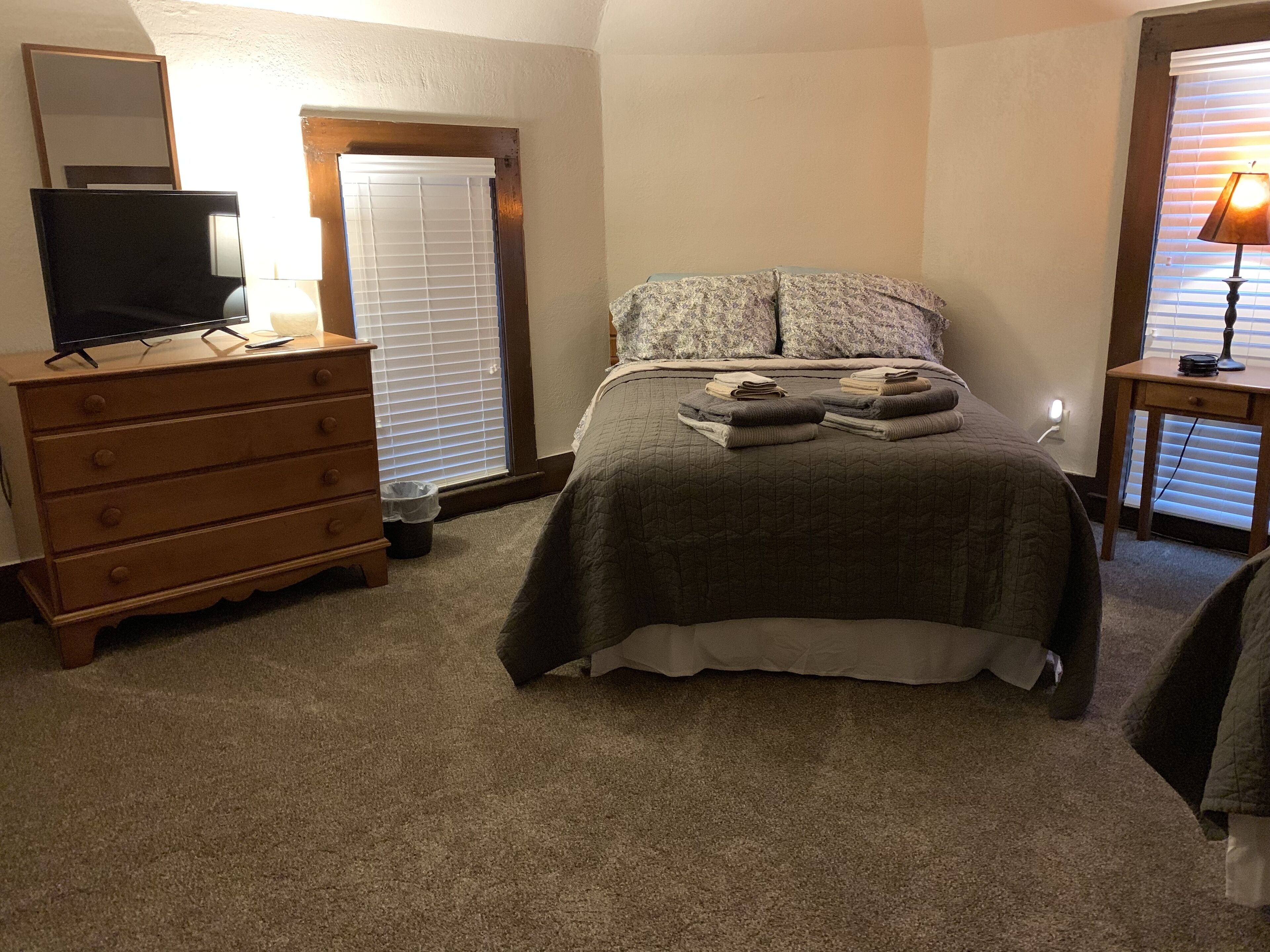 A bedroom with a bed, dresser, television, and a lamp.