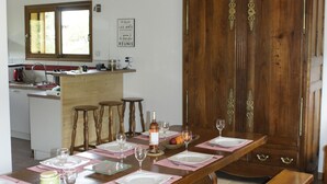 Un coin repas avec une table en bois dressée pour quatre personnes, une cuisine en arrière-plan et un grand meuble en bois.