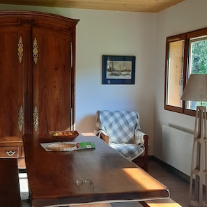 Een houten eettafel met een mand vol fruit, een stoel en een lijst met een foto aan de muur.