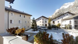 Ein verschneiter Innenhof mit Gebäuden, einem parkenden Transporter und einem Berg im Hintergrund.