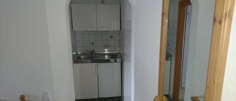 Un pasillo estrecho que conduce a una cocina con armarios blancos, un fregadero y una estufa.
