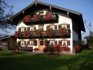 A traditional multi-story building with balconies adorned with flowers, a wooden bench, and a well-maintained lawn. - Ferienwohnung mit Dusche/WC (Nußdorf a. Inn)