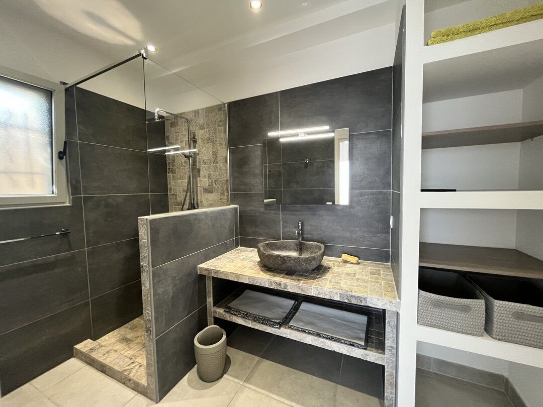 Une salle de bain moderne dotée d’une douche à parois de verre, d’un lavabo en pierre et d’étagères intégrées.