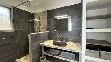 Une salle de bain moderne dotée d’une douche à parois de verre, d’un lavabo en pierre et d’étagères intégrées.