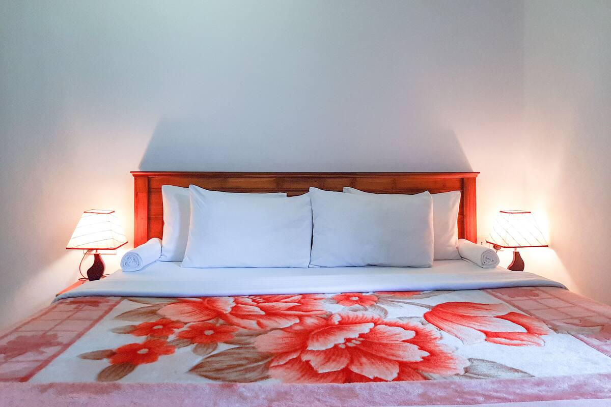 Un lit bien fait, avec du linge de lit blanc et une couvre-lit à motifs floraux, flanqué de deux lampes de chevet.