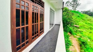 A corridor with a wooden window and a door, leading to a balcony with a view of a green hillside. - Heaven Hills Guest House (Maskeliya)