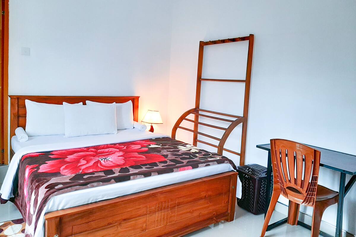 Une chambre d’hôtel avec un lit en bois, un bureau, une chaise et une poubelle.