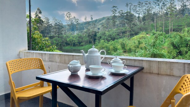 A table with tea set and chairs in a room with a view of a green landscape. - Heaven Hills Guest House (Maskeliya)