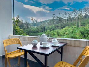 A table with tea set and chairs in a room with a view of a green landscape. - Heaven Hills Guest House (Maskeliya)