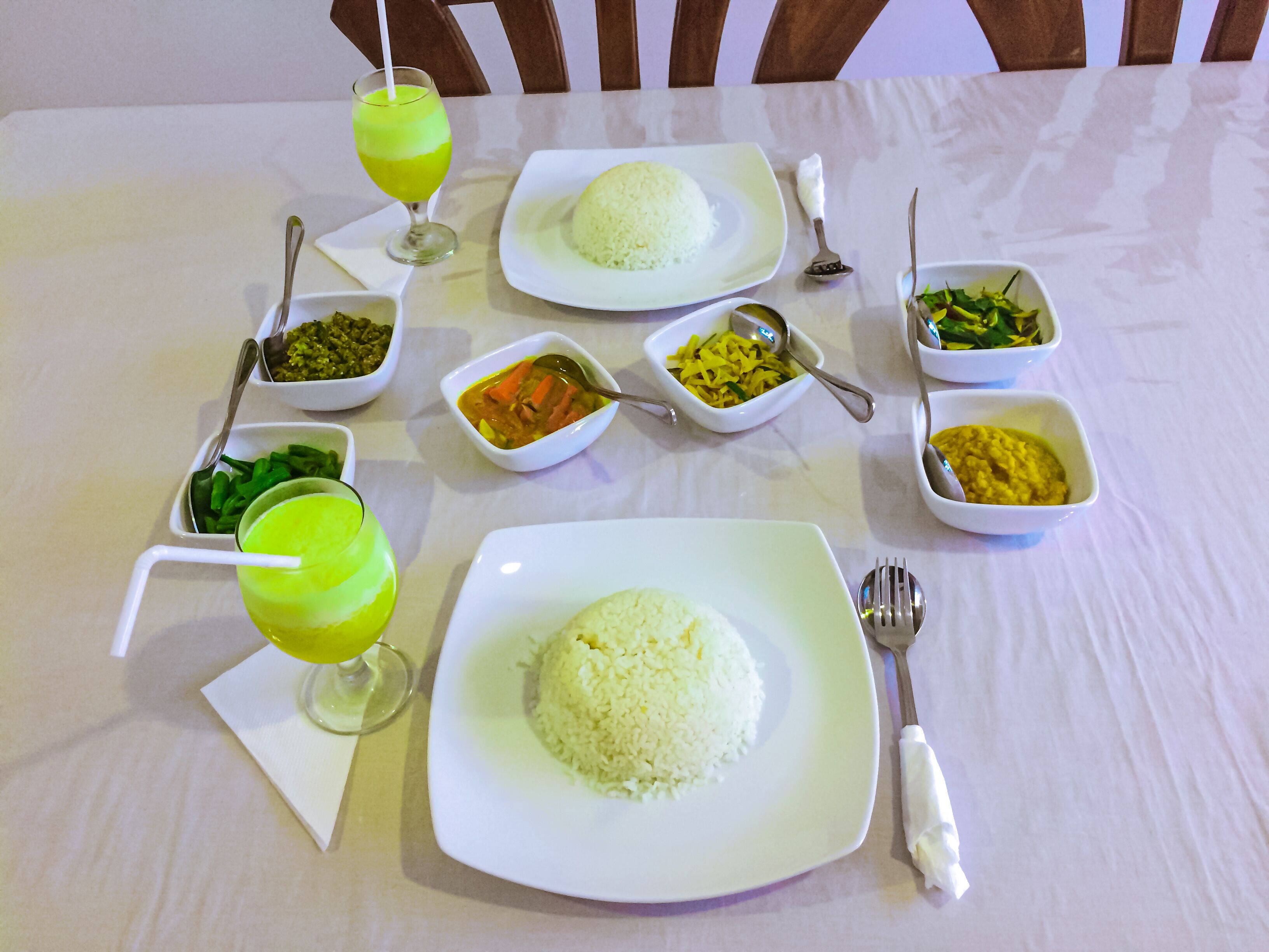 Una mesa servida con varios platos, incluyendo arroz, verduras y una bebida verde, con cubiertos y una servilleta.