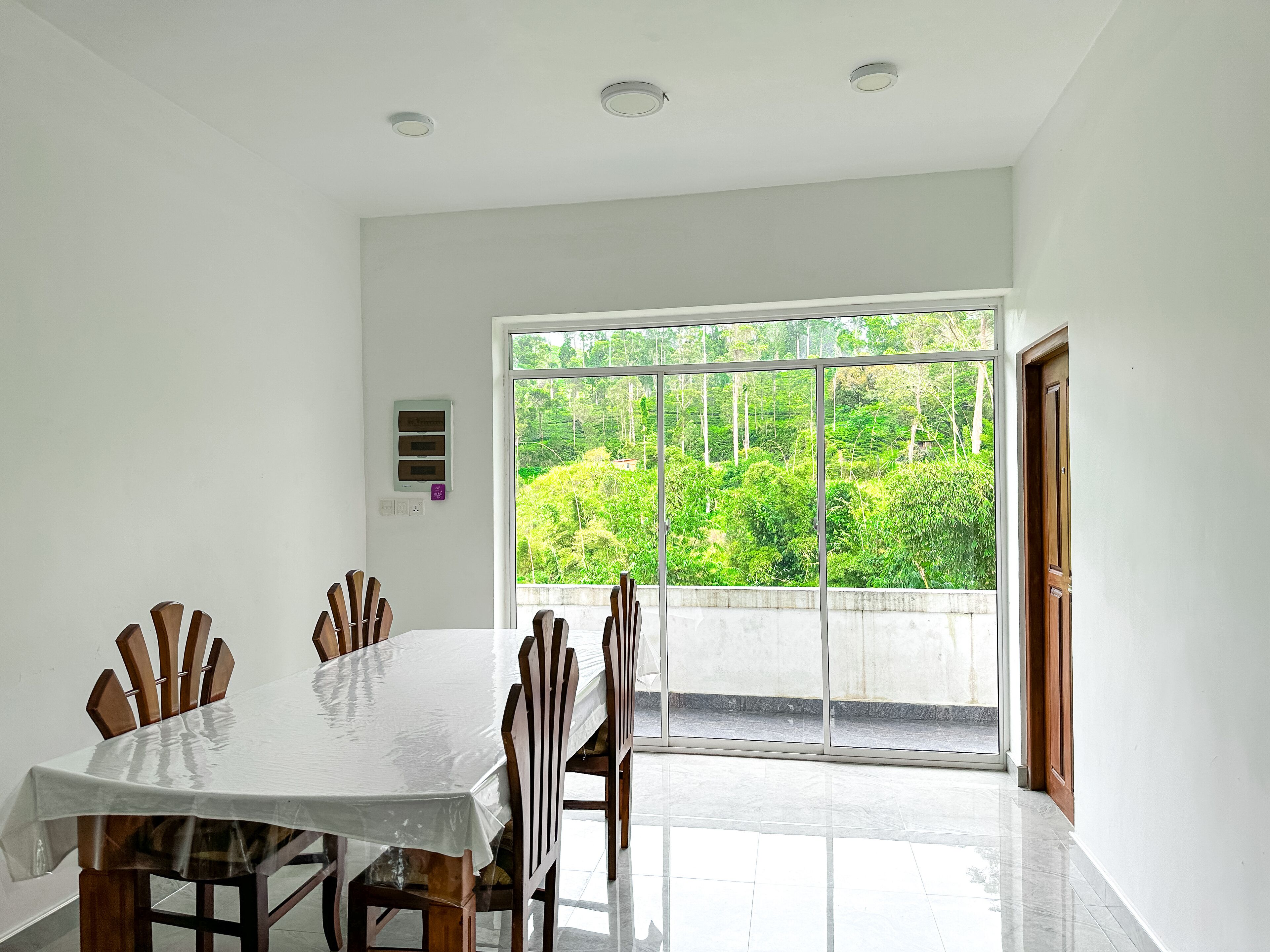 Un comedor con una mesa grande y sillas, una ventana con vista a vegetación y una puerta.