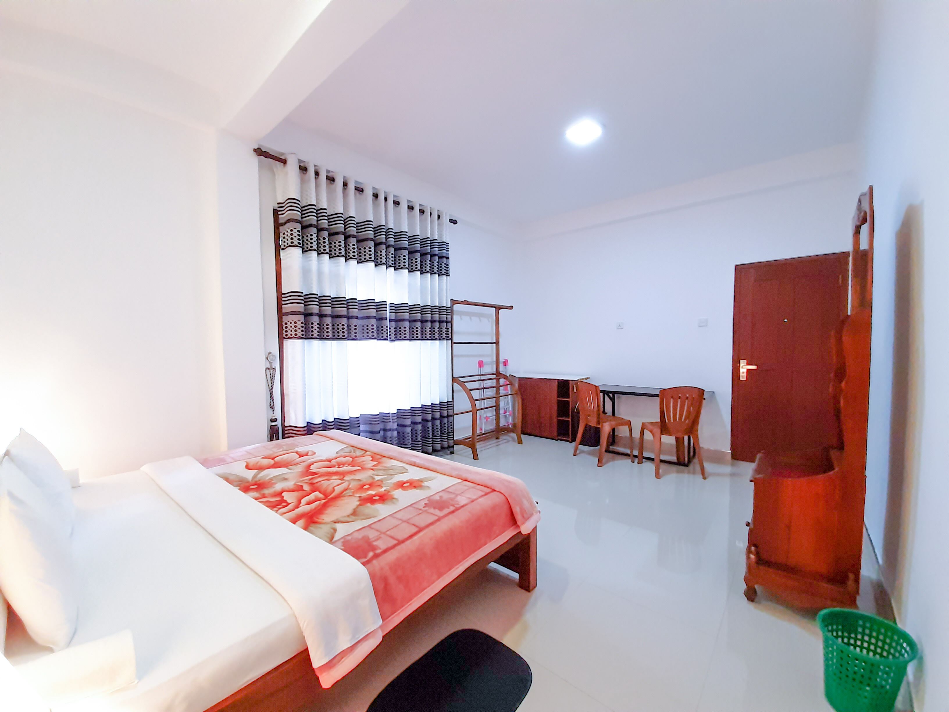 A bedroom with a bed, a desk, two chairs, a wardrobe, and a window with curtains.