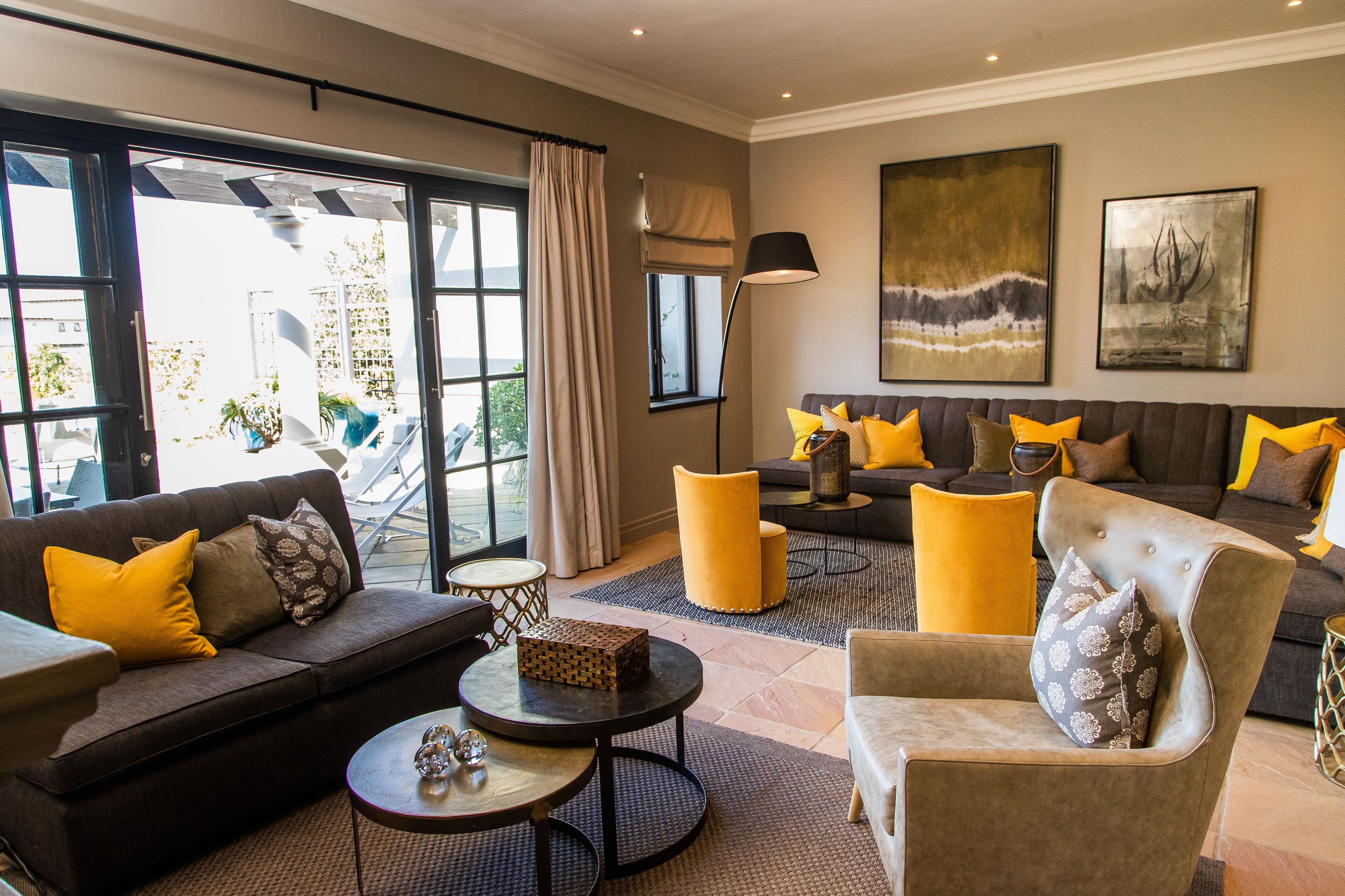 Un salon moderne comprenant un canapé, un fauteuil et une table basse, avec une grande fenêtre agrémentée de rideaux et offrant une vue sur l’extérieur.
