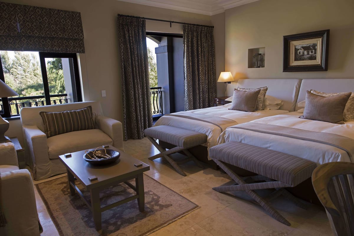 Habitación de hotel con dos camas, un sofá, una mesa y un balcón con cortinas.