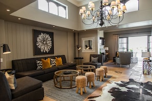A spacious living room with a high ceiling, a large chandelier, a modern sofa set, and a cowhide rug. - Sante Wellness Retreat & Spa (Paarl)
