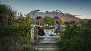 Two people sitting on a wooden deck with a view of a lake and mountains in the background. - Sante Wellness Retreat & Spa (Paarl)