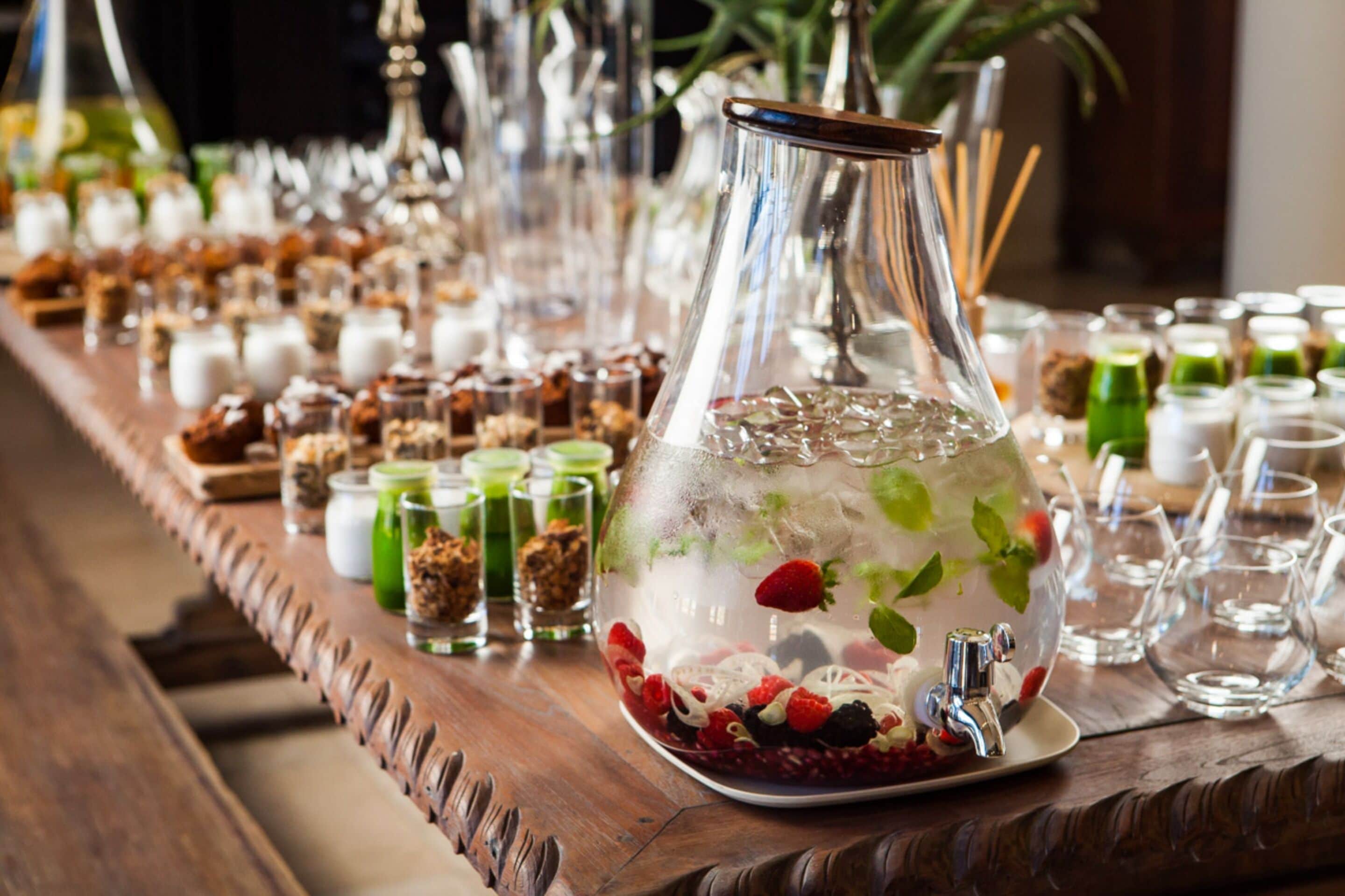 Une longue table en bois, recouverte de divers aliments, et un grand récipient en verre rempli de glace et de baies.