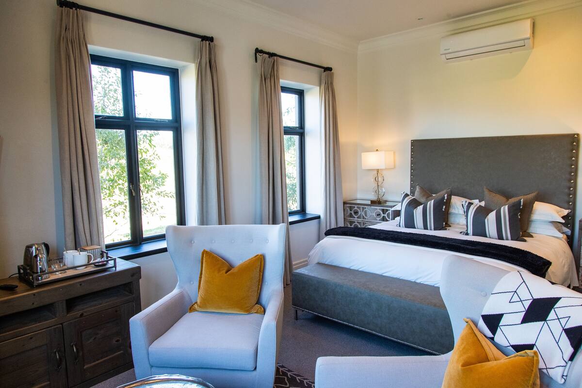 Una habitación de hotel con cama, sofá, escritorio con lámpara y ventana con cortinas.