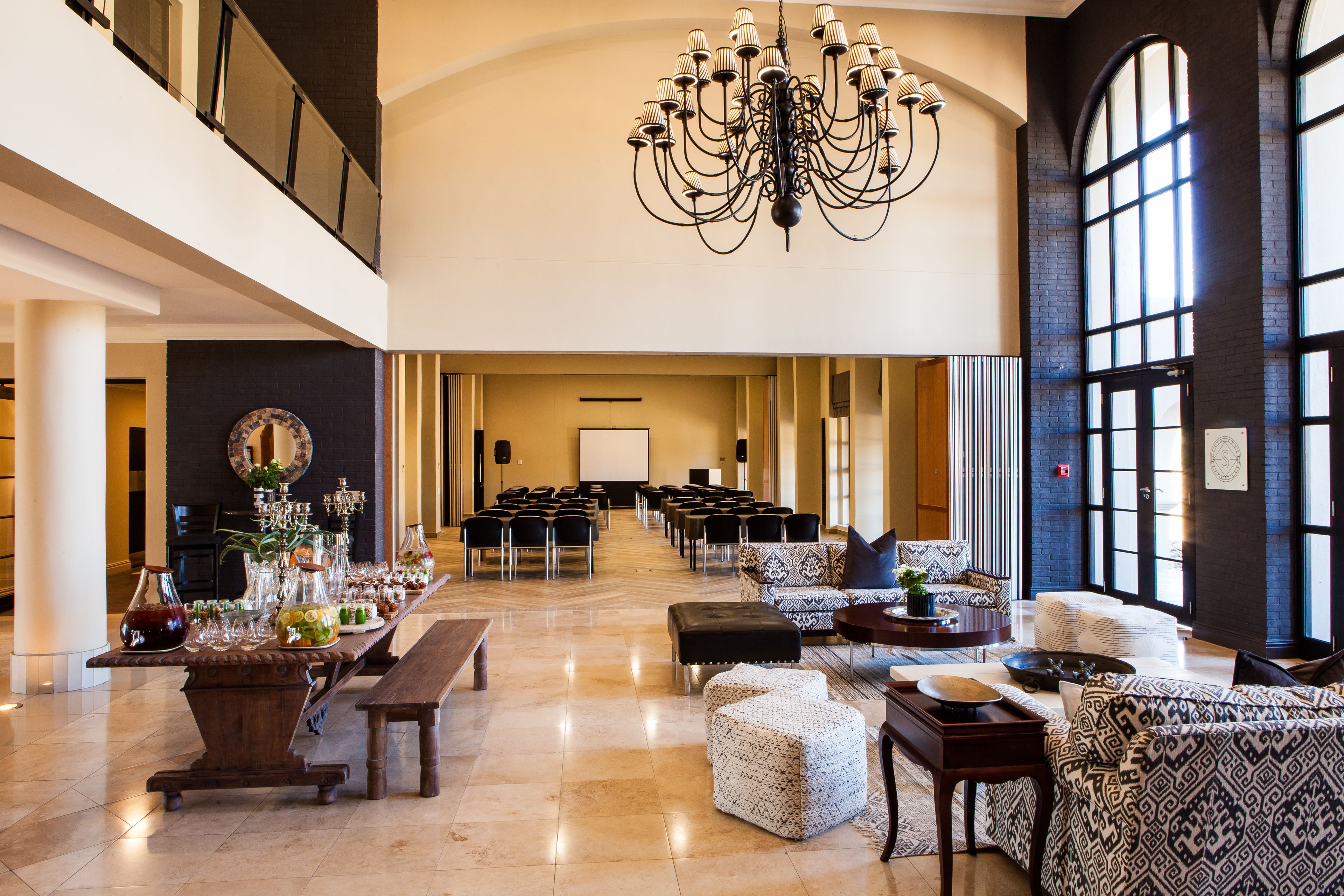 A spacious lobby with a grand chandelier, rows of black chairs, and a stage with a white screen.
