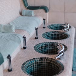 Relax in the serene spa area with a long bench and three sinks, complete with towels and a convenient towel rack.