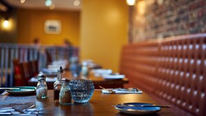 L’intérieur d’un restaurant, avec une table en bois dressée pour le repas, des salières et des poivrières, et un saladier en verre.
