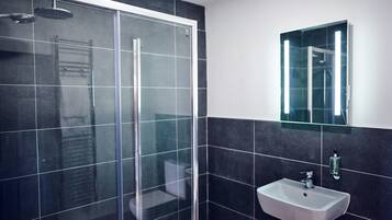 Een moderne badkamer met een douchecabine van glas, een wit wastafelmeubel en donker betegelde wanden.