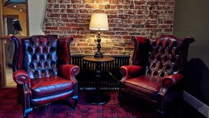 Une pièce avec deux fauteuils en cuir rouge, une petite table ronde avec une lampe et un mur en briques.