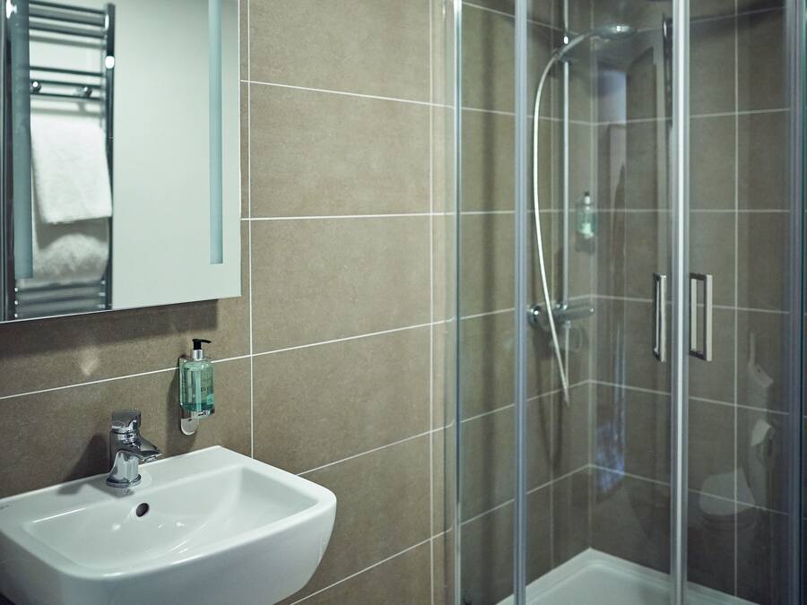 A bathroom with a glass-enclosed shower, a sink, and a mirror.