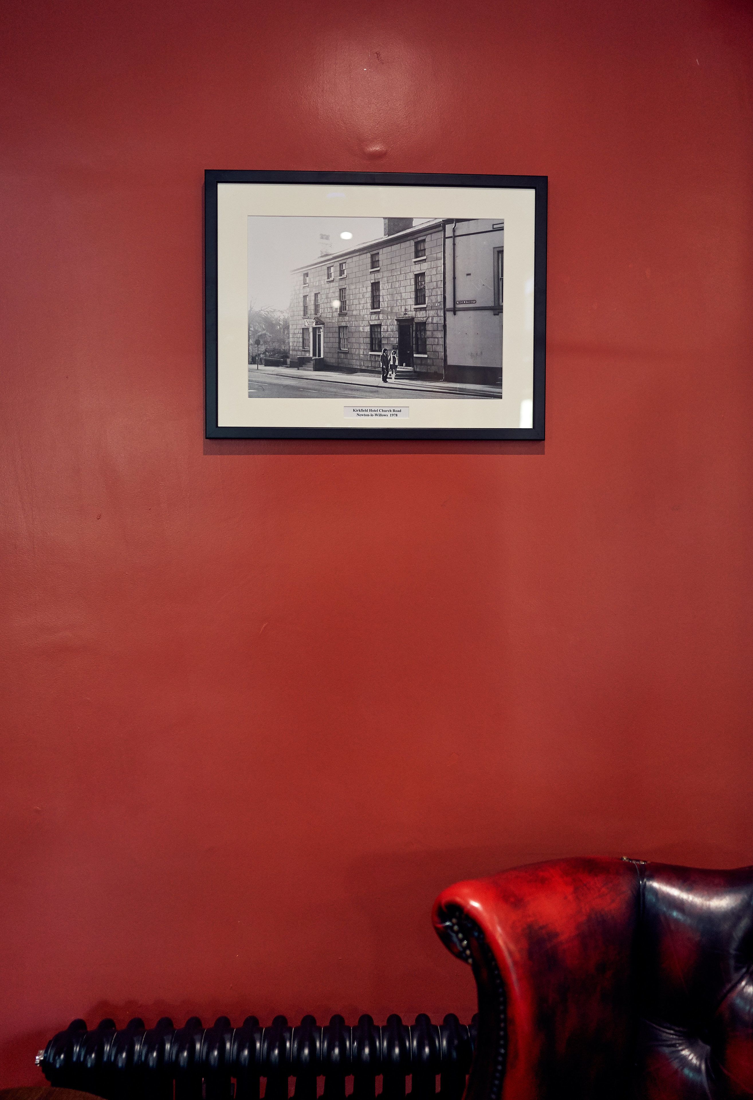 A framed black and white photograph of a building on a red wall.