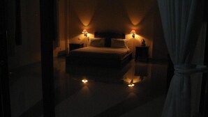 A dimly lit hotel room with a bed, two bedside lamps, and a nightstand. - Ubud Wins Bungalow (Ubud)