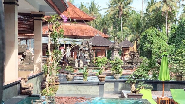 A swimming pool with a view of a traditional building and palm trees. - Ubud Wins Bungalow (Ubud)