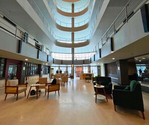 A spacious lobby with multiple seating areas, a central open space, and a high ceiling with a circular design. - Hotel Pybss (Papumpare)