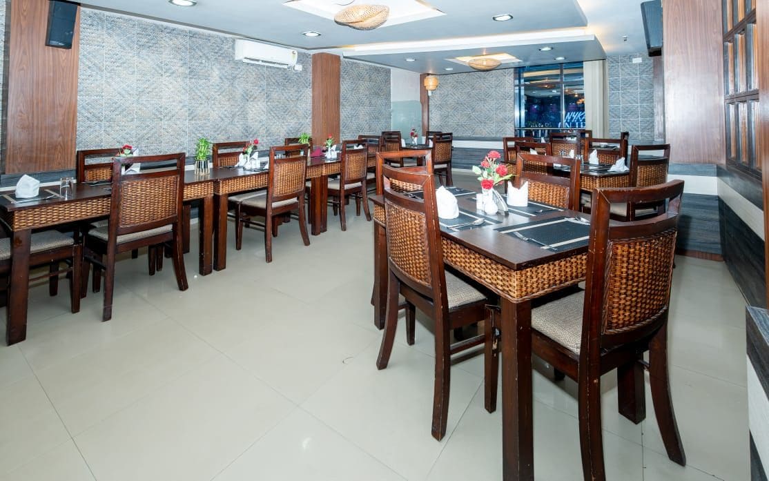 A restaurant with multiple dining tables and chairs, a stone wall, and a view of the city.