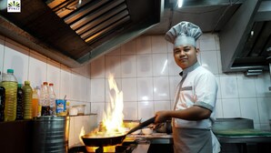 A chef cooking with a pan on a stove in a kitchen.
