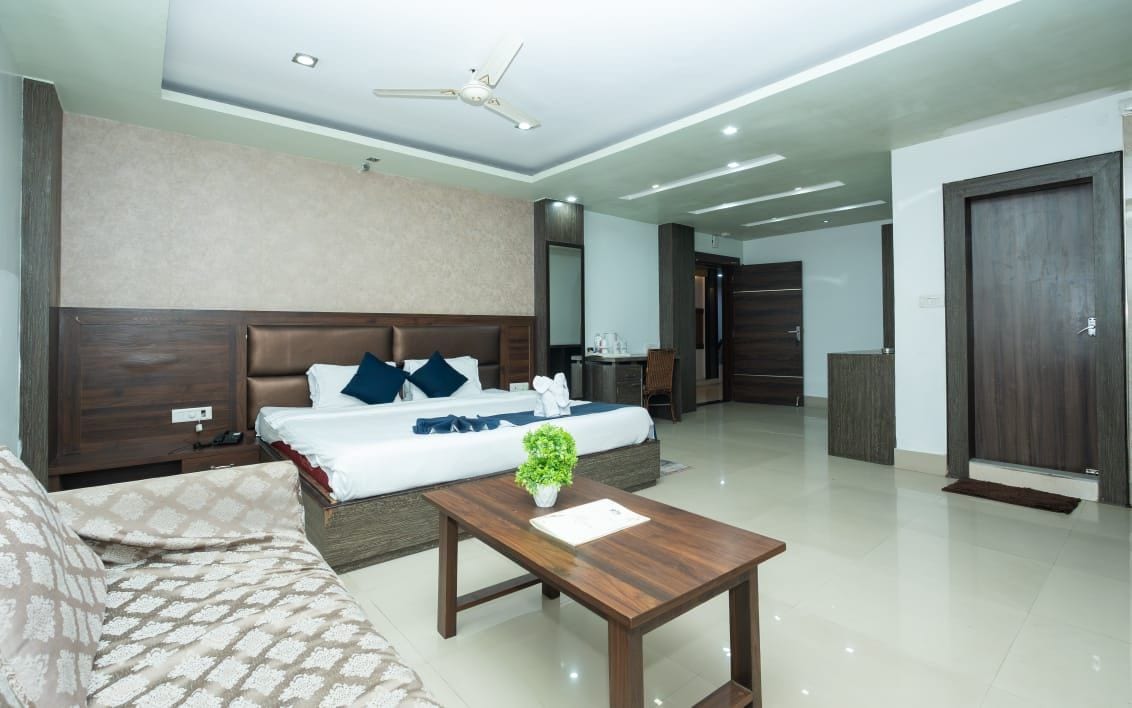 A modern hotel room with a large bed, a wooden coffee table, and a ceiling fan.