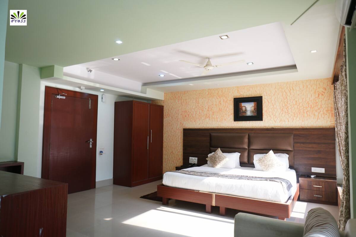 A modern hotel room with a large bed, wooden wardrobe, and a ceiling fan.
