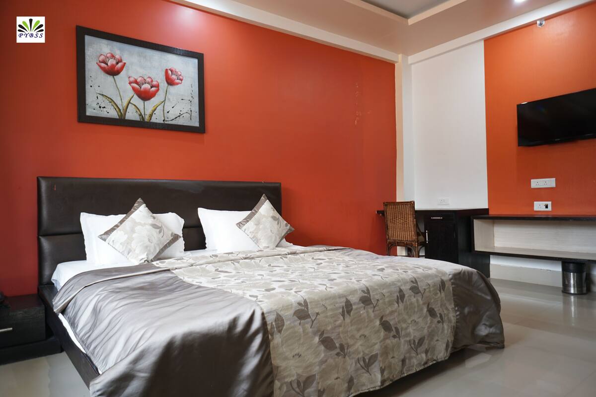 A hotel room with a bed, a television mounted on the wall, and a painting of flowers.