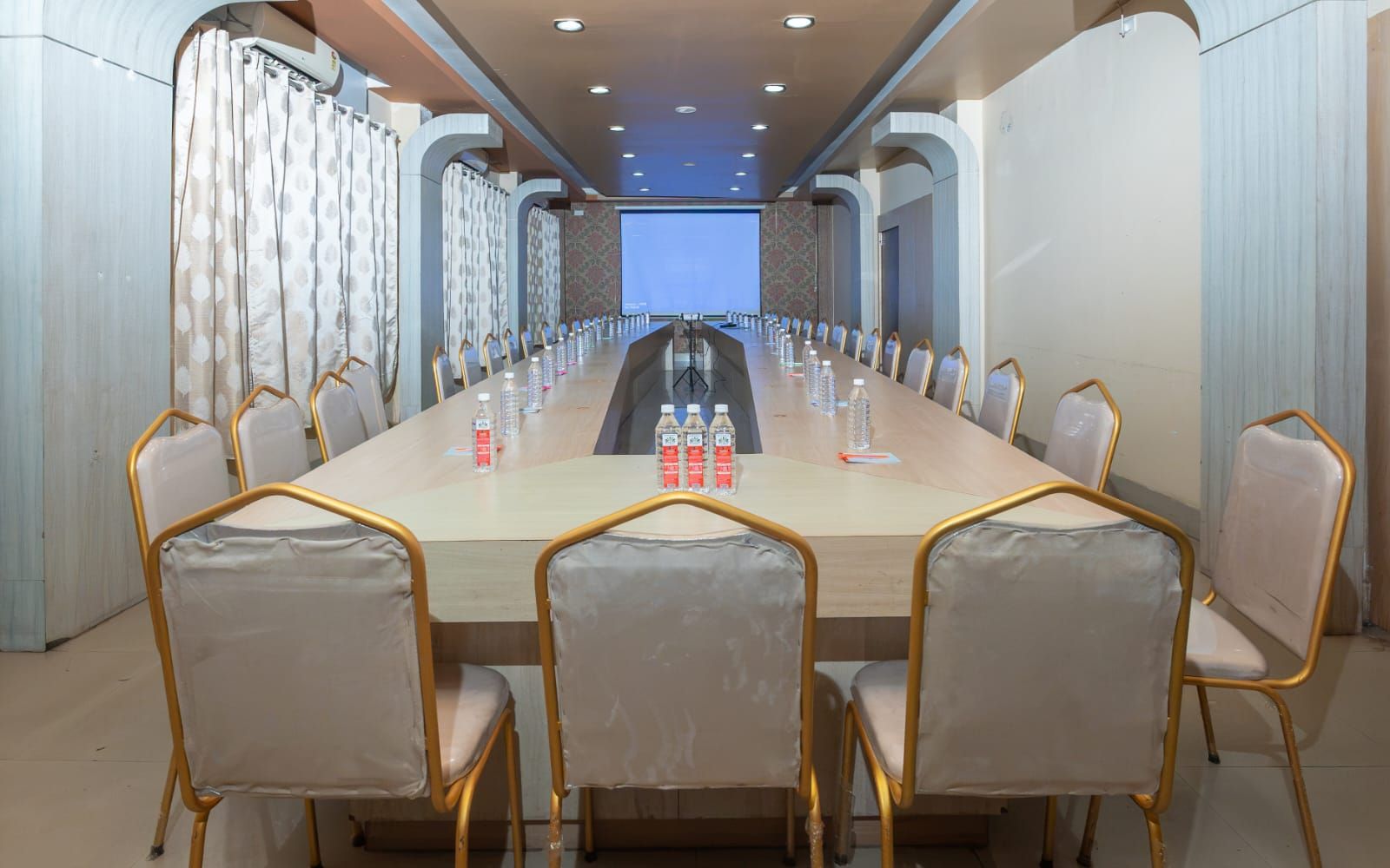 Uma sala de conferência com uma mesa comprida, cadeiras e uma tela de projeção.