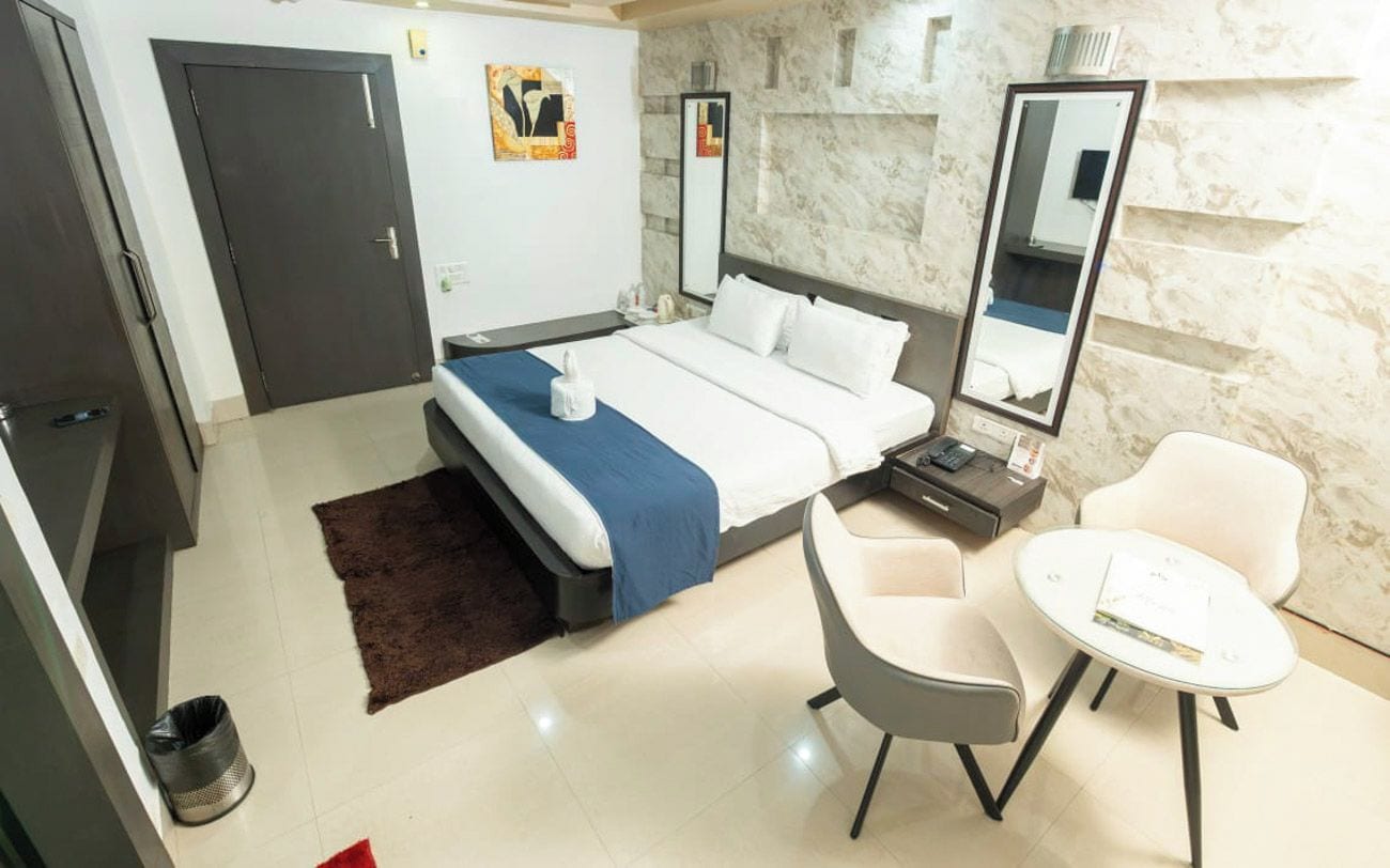 A hotel room with a bed, a chair, a small table, a mirror, and a door.