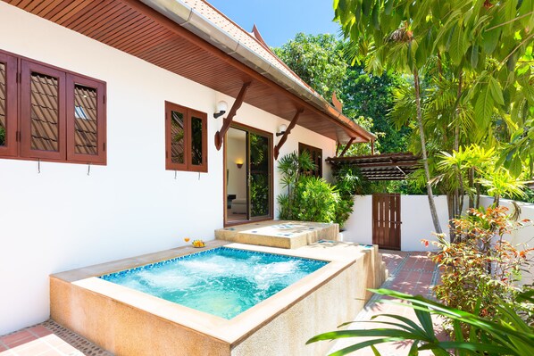 A spa area with a hot tub, a wooden deck, and a white building with brown windows. - Blissful Jacuzzi Living at Villa Nikkie2 (Rawai)