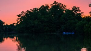 Un lago tranquilo al atardecer con un bote en primer plano y árboles densos al fondo.