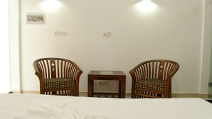 Una habitación de hotel con una cama, dos sillas de madera, una mesita y dos lámparas de pared.