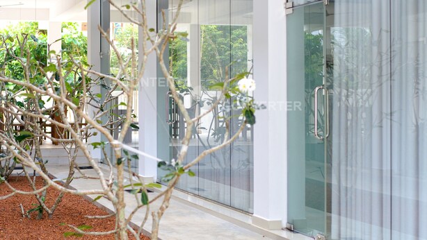 Un edificio moderno con puertas y ventanas de vidrio, piso de baldosas y un área de jardín con plantas y una bicicleta.